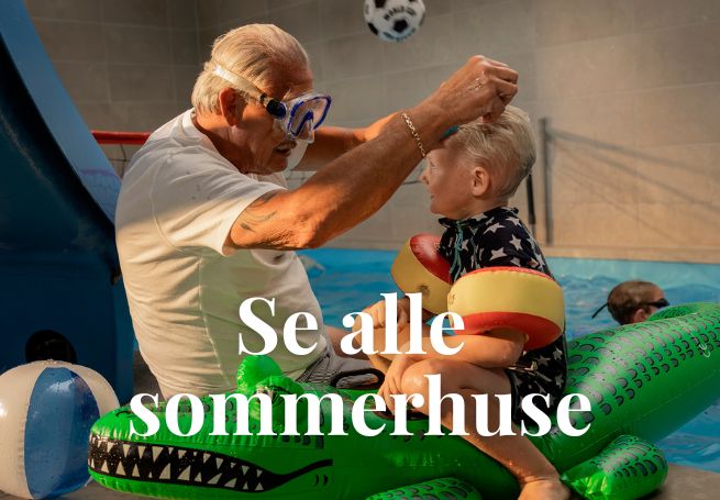Ældre mand og barn med badeudstyr sidder ved siden af indendørs pool med tekst på billede: Se alle sommerhuse